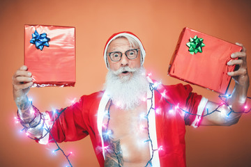 Happy Santa Claus holding Christmas presents - Hipster bearded senior having fun wearing xmas clothes celebrating holidays - Elderly people and traditional lifestyle culture