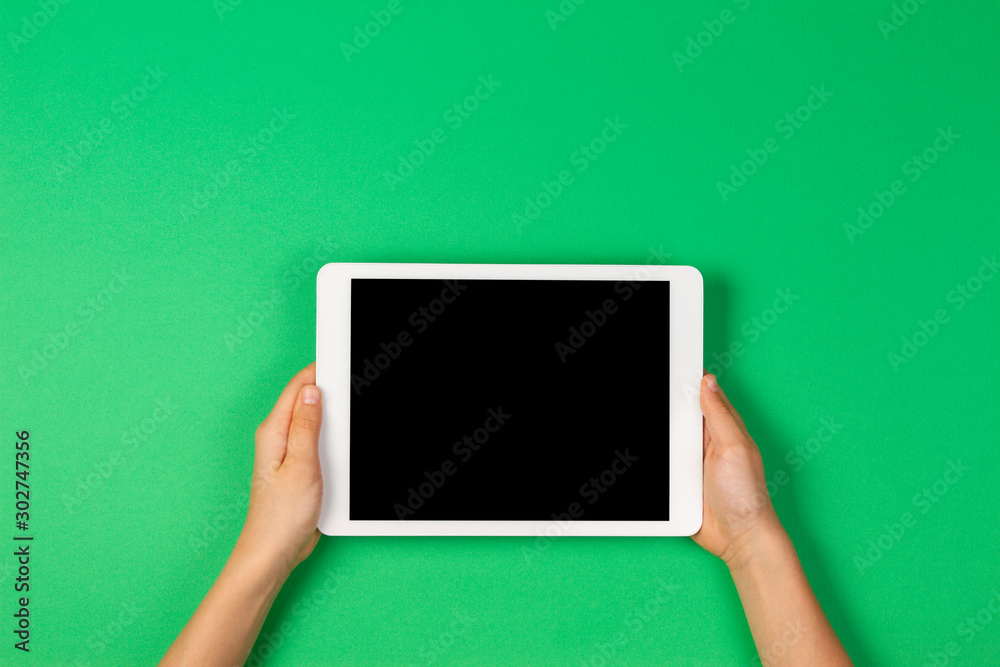 Child hands holding tablet computer on light green background - obrazy, fototapety, plakaty 