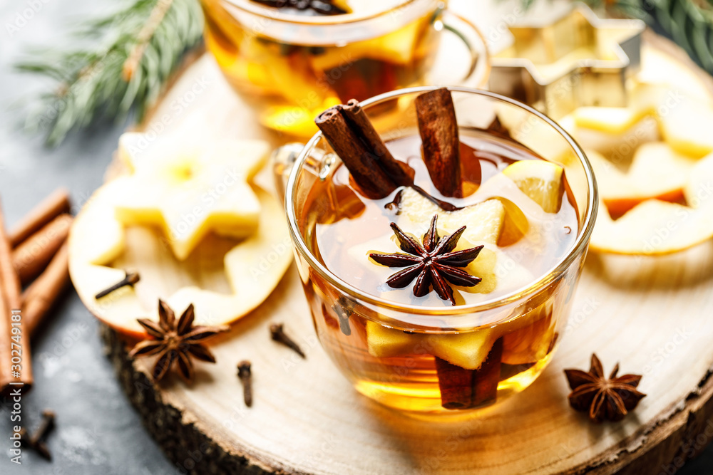 Hot drink for New Year, Christmas or autumn holidays. Mulled cider or spiced tea or mulled white wine with lemon, apples, cinnamon, anise, cloves. - obrazy, fototapety, plakaty 