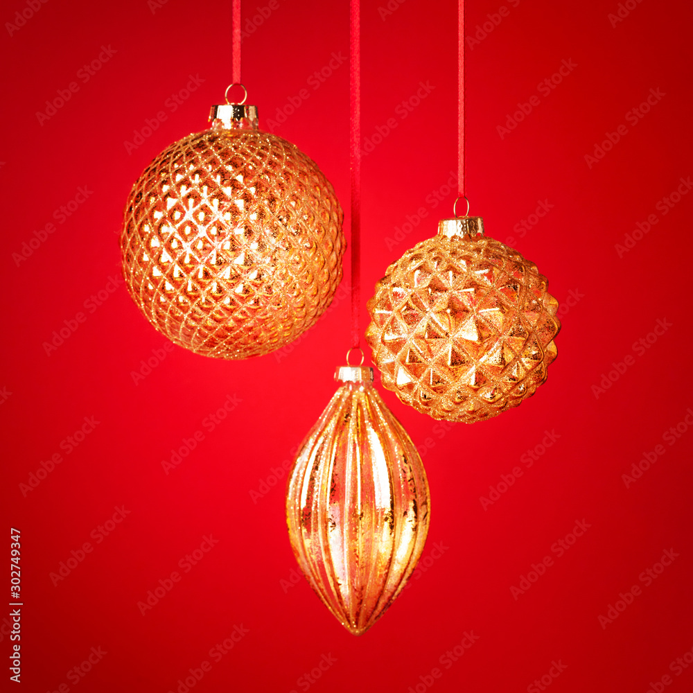 Three golden Christmas baubles hanging against the red background. New Year greeting card. Selective focus. - obrazy, fototapety, plakaty 