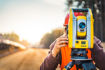 Surveyor engineer with equipment (theodolite or total positioning station) on the construction site of the road or building with construction machinery background