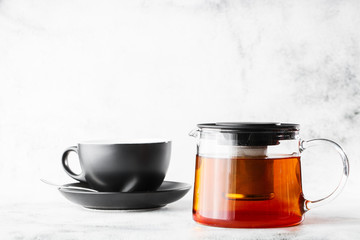 Glass teapot with dark cup of black tea isolated on bright marble background. Overhead view, copy space. Advertising for cafe menu. Coffee shop menu. Horizontal photo.