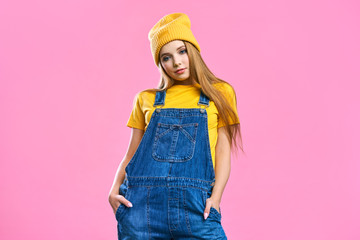 portret a pretty girl in denim overalls and a yellow hat on a pink background. fashionista lady stud