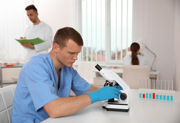 Wall Mural - Scientist with microscope at table and colleagues in laboratory. Medical research