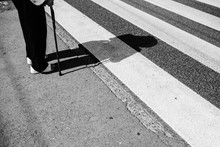 Gray Scale Shot Of A Person Holding A Cane Standing By The Zebra Crossing On The Street