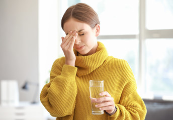 Wall Mural - Young woman with glass of water suffering from headache at home