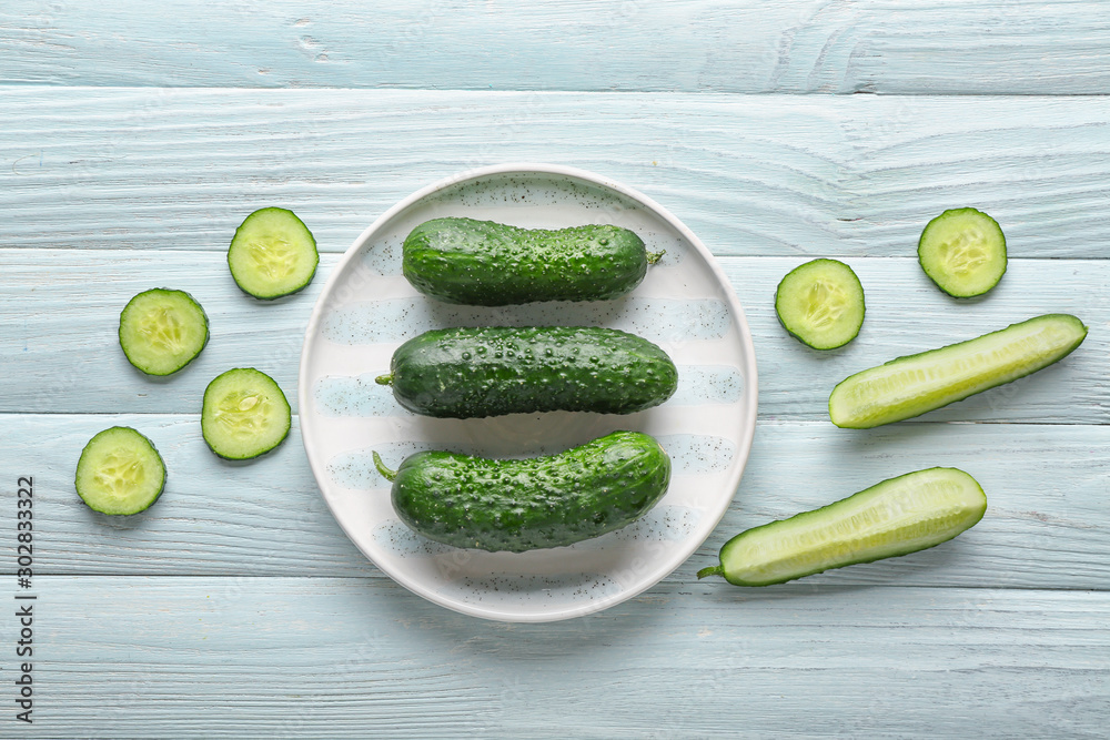 Plate with fresh cucumbers on white wooden background