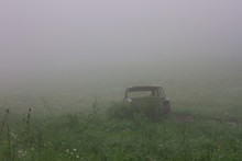 Abandoned Destroyed Car In A Green Field Covered With Fog
