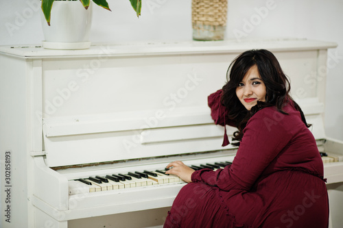 Fotografía Attractive south asian woman in deep red gown dress posed at room and play on piano