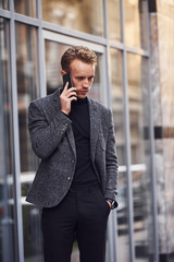 Canvas Print - Man in elegant formal wear outside against modern building talking by the phone