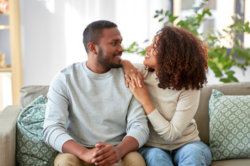 Wall Mural - relationships and people concept - happy african american couple sitting on sofa at home