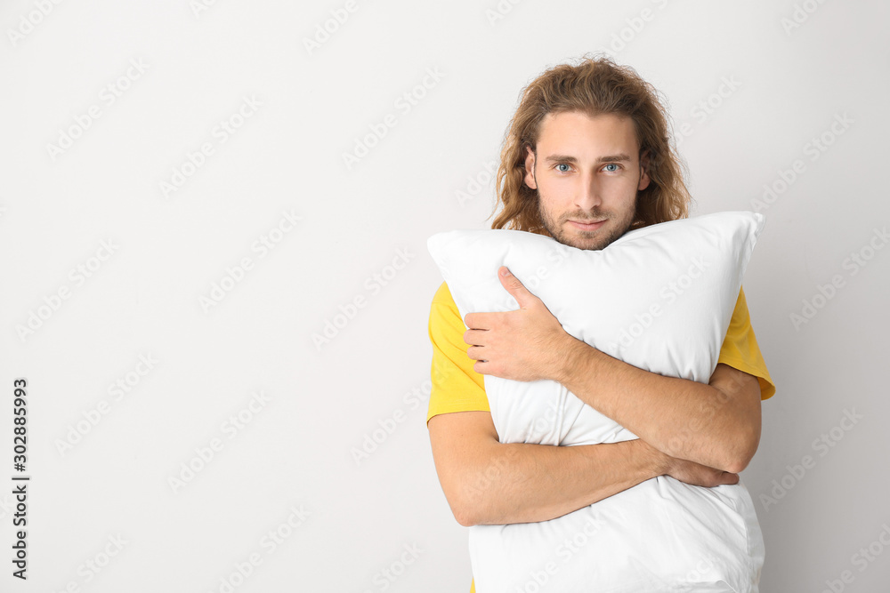 Portrait of handsome man with pillow on light background