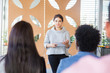© Mangostar - Serious female student presenting project to classmates. Young woman in casual speaking before audience in training room, holding paper with notes. Presentation concept