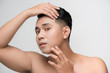 © makistock - Portrait of shirtless young handsome Asian man checking his face for skin care and beauty concepts