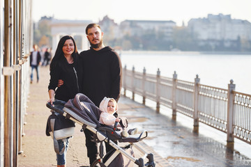 Wall Mural - Cheerful family with pram have a walk together with their child in the park