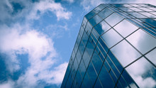 Futuristic Business. Low Angle View Of A Glass And Steel Skyscraper Blending Into And Reflecting The Blue Sky And Clouds.