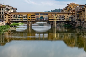 Wall Mural - Ponte Vecchio bridge in the foreground of high buildings reflected in the lake in Florence, Italy