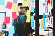 © BullRun - Positive man in optical spectacles with cute smile on face making notes on paper sticks during collaboration with colleagues, happy crew of professional people searching ideas for startup project