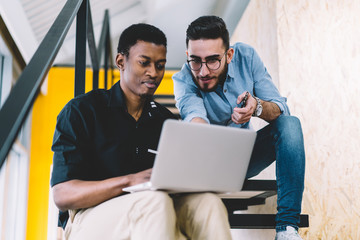 Two male friends making research of  content websites on netbook, multicultural men office employees sharing ideas while developing website on laptop computer. Caucasian and African American student