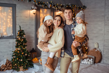 Happy family of 4 in anticipation of the New Year holiday having fun in the snow near the veranda of a wooden house.