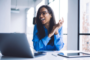 Joyful black woman clasping looking at monitor with smile