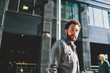 © BullRun - Portrait of handsome bearded young man in denim wear standing outdoors on street of business town and looking at camera.Good looking hipster guy walking in urban setting near modern mall