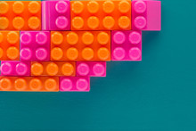 Pink And Orange Blocks Of A Children's Designer Of Various Shapes On A Green Background Laid Out By A Ladder In The Upper Left Corner Of The Image. Copy Space. Flat Lay
