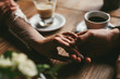 © VlaDee - Bride and groom holding hands on wooden table indoor cafe