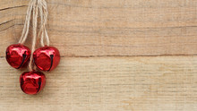 Three Red Jingle Bells Hanging On Rope Against A Wood Background With Writing Space