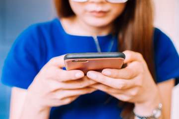 A young Asian woman in casual attire is using a smart phone indoor