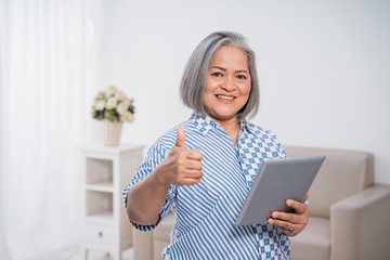 Wall Mural - Old woman confident with thumbs up using tablet when handling her business