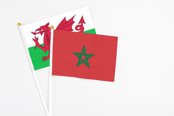 Morocco and Wales stick flags on white background. High quality fabric, miniature national flag. Peaceful global concept.White floor for copy space.