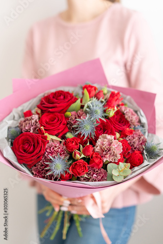 Mixed bouquet of red tones. Beautiful bunch of fresh flowers in womans hands. The work of the florist at a flower shop. Fresh cut flower. © malkovkosta