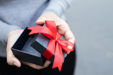 Wall Mural - female hands holding open gift box dark black wrapped pack with beautiful red ribbon. for surprise special event with copy space. Christmas, birthday or new year concept. High resolution product.