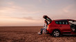 Young Happy Couple Dressed Alike in White Shirt and Jeans Sitting at Their New Car Trunk, Beautiful Sunset on the Field, Vacation and Travel Concept