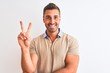 Young handsome man wearing elegant t-shirt over isolated background smiling with happy face winking at the camera doing victory sign. Number two.