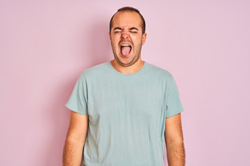 Sticker - Young man wearing blue casual t-shirt standing over isolated pink background sticking tongue out happy with funny expression. Emotion concept.