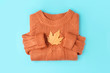 Yellow autumn leaf on orange knitted sweater background, top view flat lay.