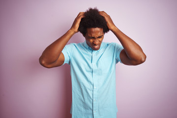 Poster - Young american man with afro hair wearing blue shirt standing over isolated pink background suffering from headache desperate and stressed because pain and migraine. Hands on head.