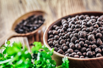 Wall Mural - Black pepper. Pile of black pepper in wooden bowl. Wood spoon. full of pepper in background with green leaf.