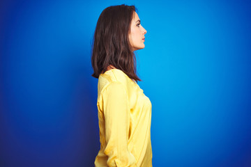 Wall Mural - Young beautiful woman wearing yellow t-shirt standing over blue isolated background looking to side, relax profile pose with natural face with confident smile.