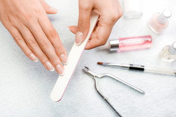 Woman holding nails file in her fingers. Manicure items like brush lacquer, nail varnish remover, scissors in background.