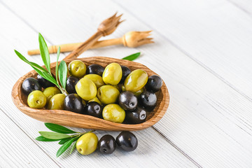 Wall Mural - Fresh green and black olives on white background. Olive mix in wooden bowl from top view on rustic board with copy space.