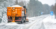 Snow Plow On Highway Salting Road. Orange Truck Deicing Street At Snowing Time. Crystals Dropping On Asphalt. Maintenance Winter Vehicle In Action.