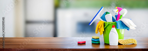 Fotografía Bucket with cleaning items on wooden table and blurry modern kitchen background