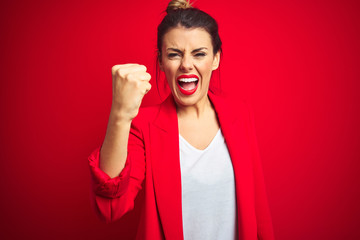 Poster - Young beautiful business woman standing over red isolated background angry and mad raising fist frustrated and furious while shouting with anger. Rage and aggressive concept.