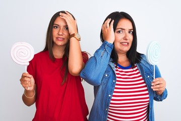 Wall Mural - Young beautiful women holding sweet lollipop standing over isolated white background stressed with hand on head, shocked with shame and surprise face, angry and frustrated. Fear and upset for mistake.