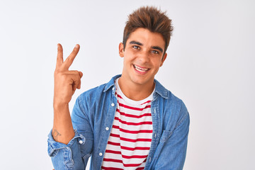 Young handsome man wearing striped t-shirt and denim shirt over isolated white background smiling with happy face winking at the camera doing victory sign. Number two.