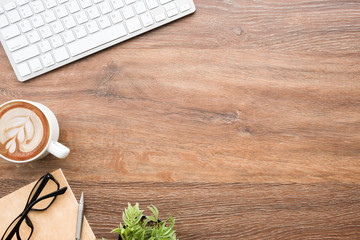 Wood office desk table with computer keyboard, cup of latte coffee and supplies. Top view with copy space, flat lay.