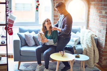 Wall Mural - Young beautiful couple smiling happy and confident. Woman surprise man with gift around christmas decoration at home